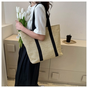 French style woven tote bag with black handles held by model in a minimalist setting