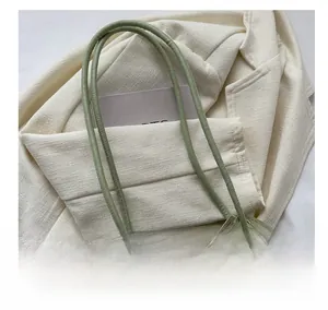 Détail d'un sac tressé montrant la poignée en cuir vert olive et le connecteur en métal