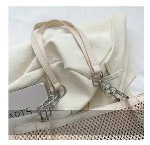 Detail showing the woven texture and metal chain link handle of this beige tote bag