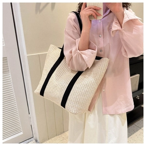 Close-up of woven straw tote bag with black canvas straps for summer beach travel use