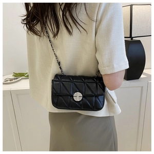 Detail of black quilted crossbody bag with silver clasp and chain strap on a model