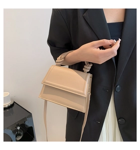 Detailed close-up of beige leather crossbody bag with twisted handle and flap closure
