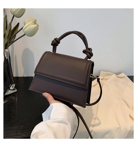 Detail of a dark brown PU leather handbag with a unique knotted handle on a desk
