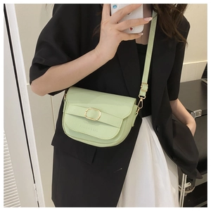 Détail du sac besace en cuir vert clair avec boucle dorée et texte embossé