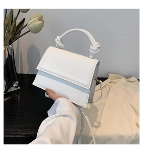 Detail view of a white minimalist handbag featuring a modern knotted handle and leather texture