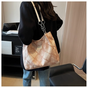 Close-up of a large plaid tote bag with chain strap worn by a model in a blazer