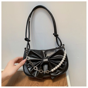 Détail du sac à bandoulière noir avec nœud décoratif et chaîne de fleurs en perles