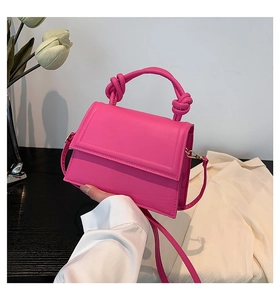 Close-up of magenta handbag with knotted handle detail held by hand on elegant background