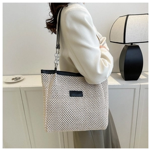 Detail of cream woven tote bag with black leather trim and silver chain shoulder strap