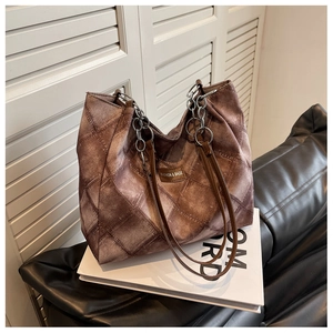 Detail of quilted brown tote bag with metal chain strap and fashion label on front