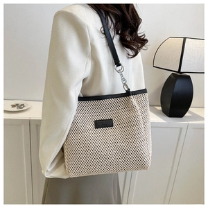 Detail of woven tote bag with black leather trim and embossed brand patch on the side