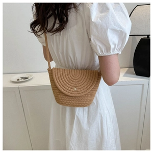 Détail d'un sac bandoulière en paille tissée avec fermoir doré porté sur une robe blanche