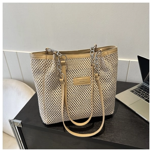 Close-up of woven tote bag with leather straps and silver chain details on a desk