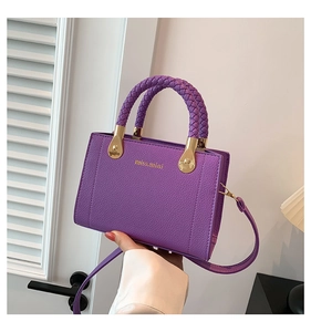 Gros plan du sac à main violet en cuir litchi avec poignée tressée et logo doré