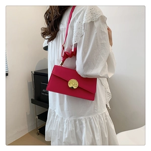 Detail of rose red shoulder bag featuring a large gold metal buckle and pleated strap