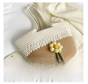 Detail showing two-tone straw tote bag with crochet flower charm next to a phone for size