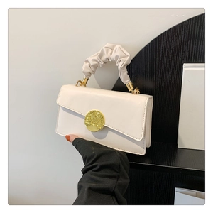 Detail of cream white pleated handle handbag with textured golden circular metal buckle