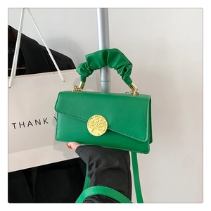 Detail view of green pleated handle handbag with gold coin accent and asymmetric flap