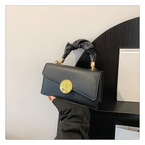 Detail of minimalist black pleated handbag featuring matte metal buckle and smooth texture