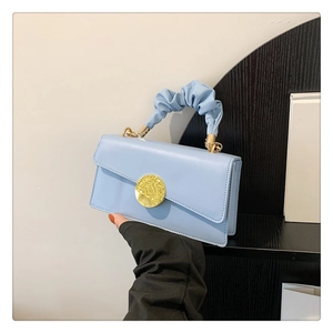 Close-up of light blue pleated handle handbag with a round golden metal buckle