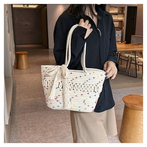 Detail of cream woven tote bag featuring colorful dots and lace bowknot pendant accessory