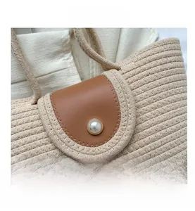 Détail du sac cabas tissé beige avec rabat en cuir marron et grande perle décorative