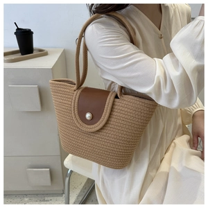 Détail du sac cabas tissé main avec rabat en cuir brun et grande perle sur texture beige