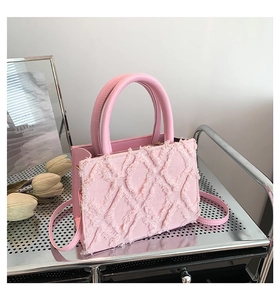 Detail view of pink quilted denim handbag with frayed edges on a metal shelf
