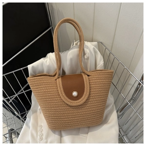 Détail d'un sac cabas en paille tressée avec rabat en cuir et élégante perle de fermeture