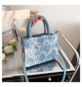 Detailed close-up of light blue denim tote bag with frayed diamond quilting on metal shelf