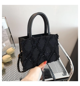 Detail of black fringe tote bag showing diamond texture and gold hardware accents