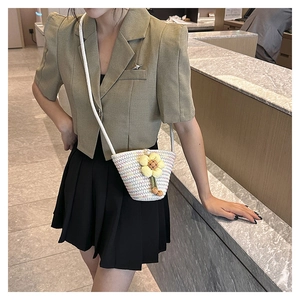 Detail of beige straw crossbody bucket bag featuring a vibrant yellow fabric flower accent