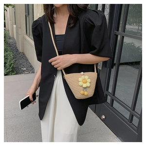 Straw shoulder bag with yellow flower decor and pearl clasp shown in outdoor scene