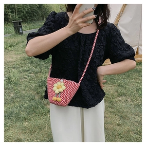 Outdoor shot of a woven crossbody bucket bag featuring red houndstooth and a yellow flower