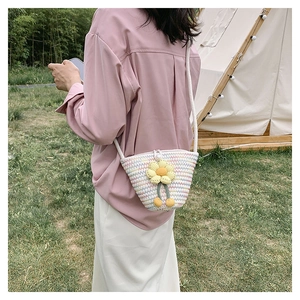 Outdoor shot of a woven bucket bag with sunflower detail and white pearl clasp
