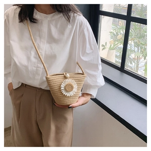 Détail du sac seau en paille tressée avec fleur de marguerite blanche et fermoir perle