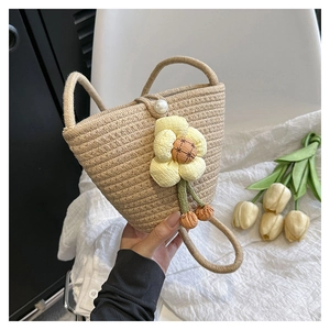 Detailed shot of khaki woven bucket bag featuring yellow fabric flower and pearl clasp detail