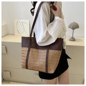 Detail of large woven straw tote bag with brown leather patchwork in a lifestyle setting