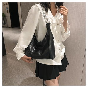 Sac hobo noir brillant avec bandoulière chaîne porté par un mannequin en chemise
