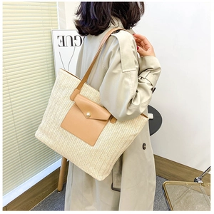 Detail of straw woven tote bag featuring a brown leather pocket and pearl buckle