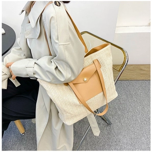 Detail of a large straw tote bag with brown leather pocket and elegant pearl accent