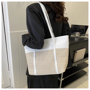 Detail of minimalist woven straw tote bag featuring contrast stitching and large capacity