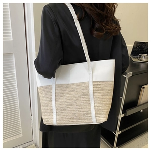 Detail of a large straw tote bag with white leather patchwork on a model in a black suit
