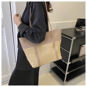 Detail of a large straw tote bag with leather patchwork shown on a model in a modern room
