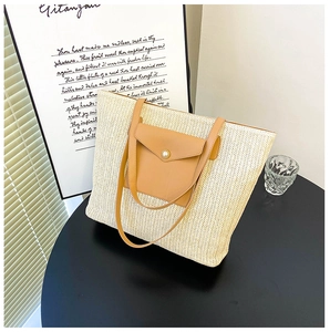 Detail of woven straw tote bag featuring brown leather pocket and white pearl button