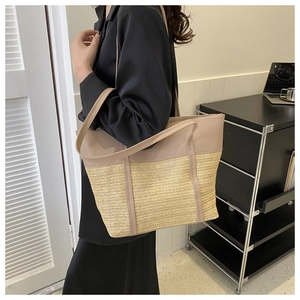 Detail of a large straw tote bag with beige leather stitching and shoulder straps