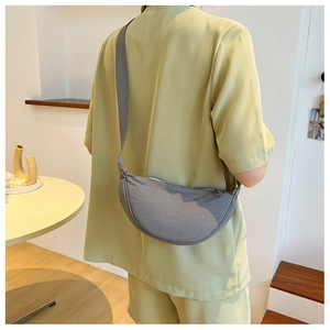 Detail of grey crescent shoulder bag worn with a light green suit in a modern room