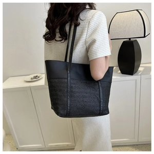 Detail of a black woven tote bag with smooth leather patchwork shown on model's shoulder