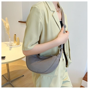 Side view of a grey nylon crescent crossbody bag on a model wearing a green suit