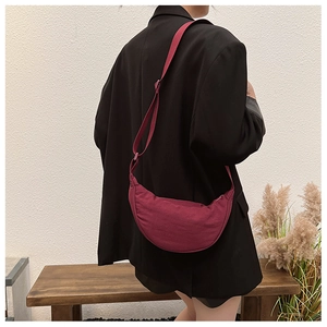 Detail of burgundy half-moon crossbody bag with adjustable strap on a chic model